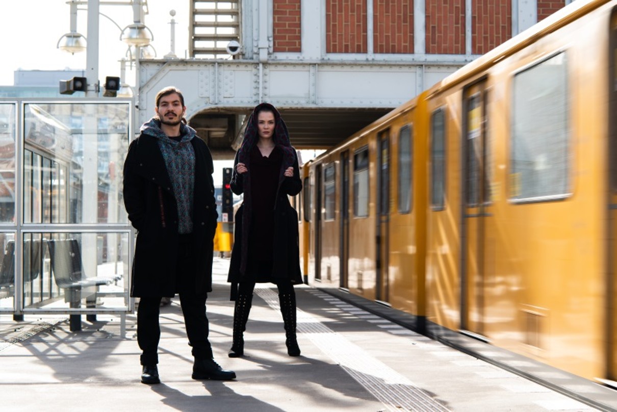 Zwei Personen in dunkler Kleidung neben einer einfahrenden S-Bahn.