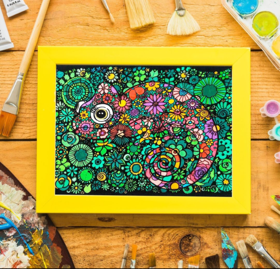 Ein Ausmalbild mit einem Chamäleon-Motiv umgeben von Pinseln und Farben.