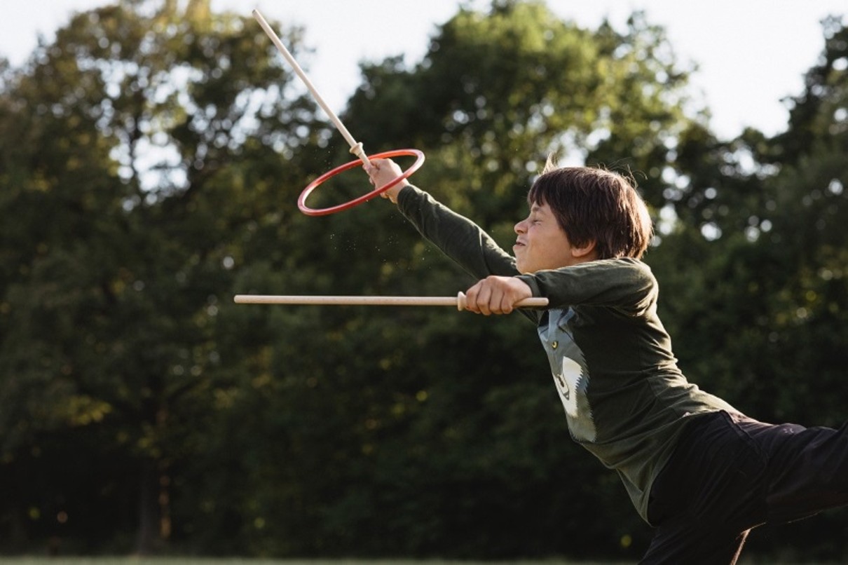  A boy playing with a stick and ring, with trees in the background.