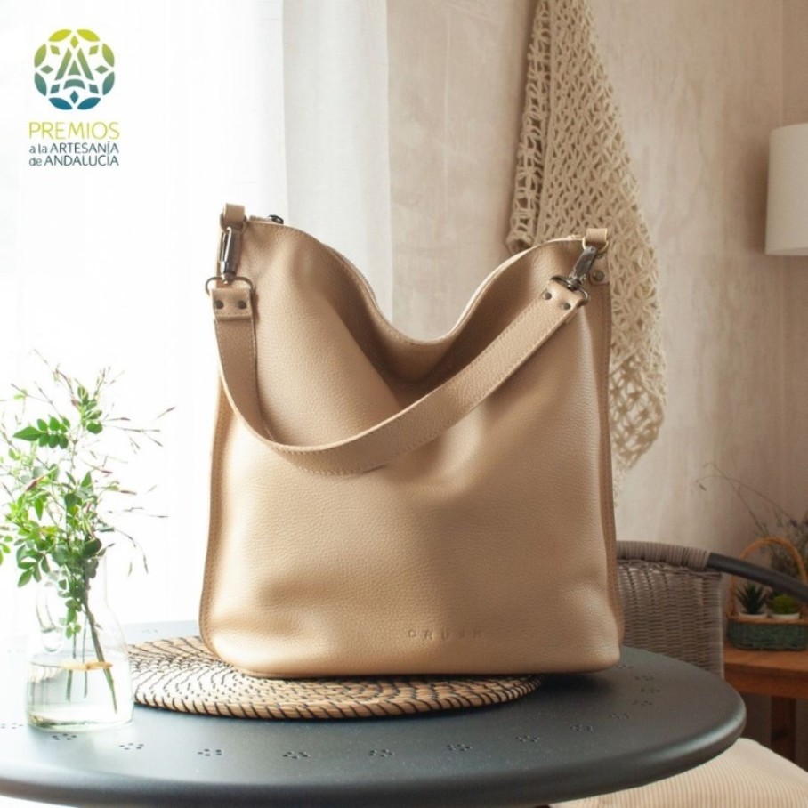 A beige leather bag on a metal table, next to it a plant in a vase. 