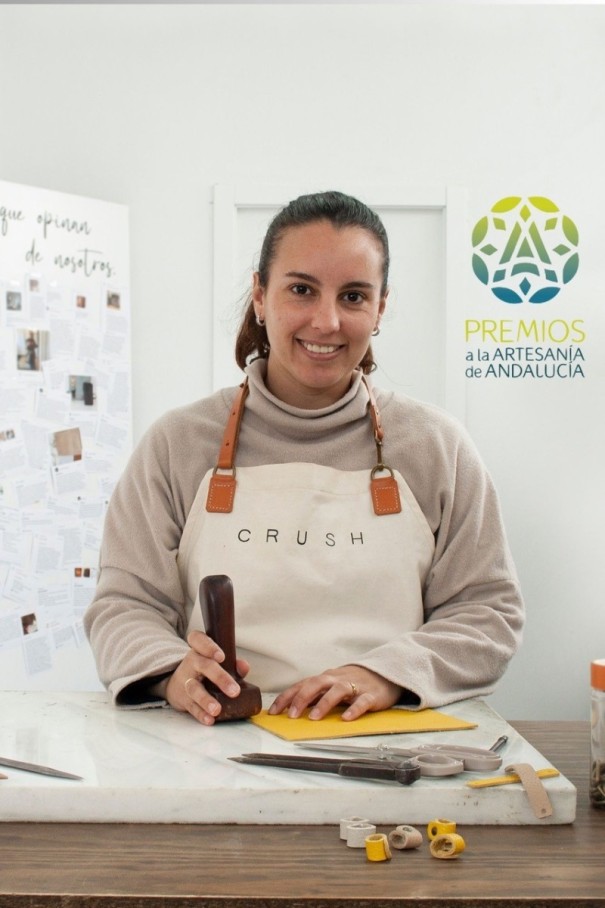 : A woman looking into the camera. In her right hand she holds a wooden tool. 