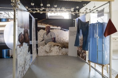 Large photo walls with an image of a woman surrounded by cotton, pieces of clothing hang in front of the walls. 