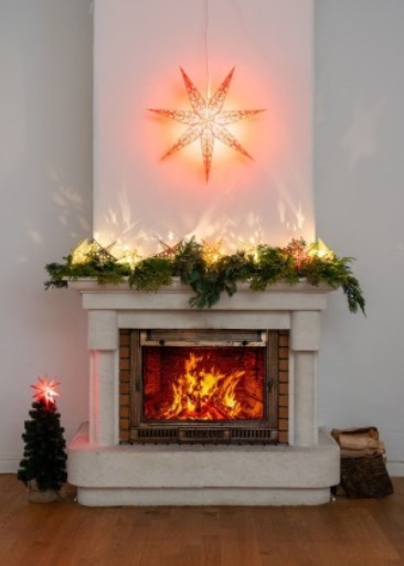 Einen Kamin mit weihnachtlicher Dekoration, darunter ein leuchtender Stern und Lichterketten.