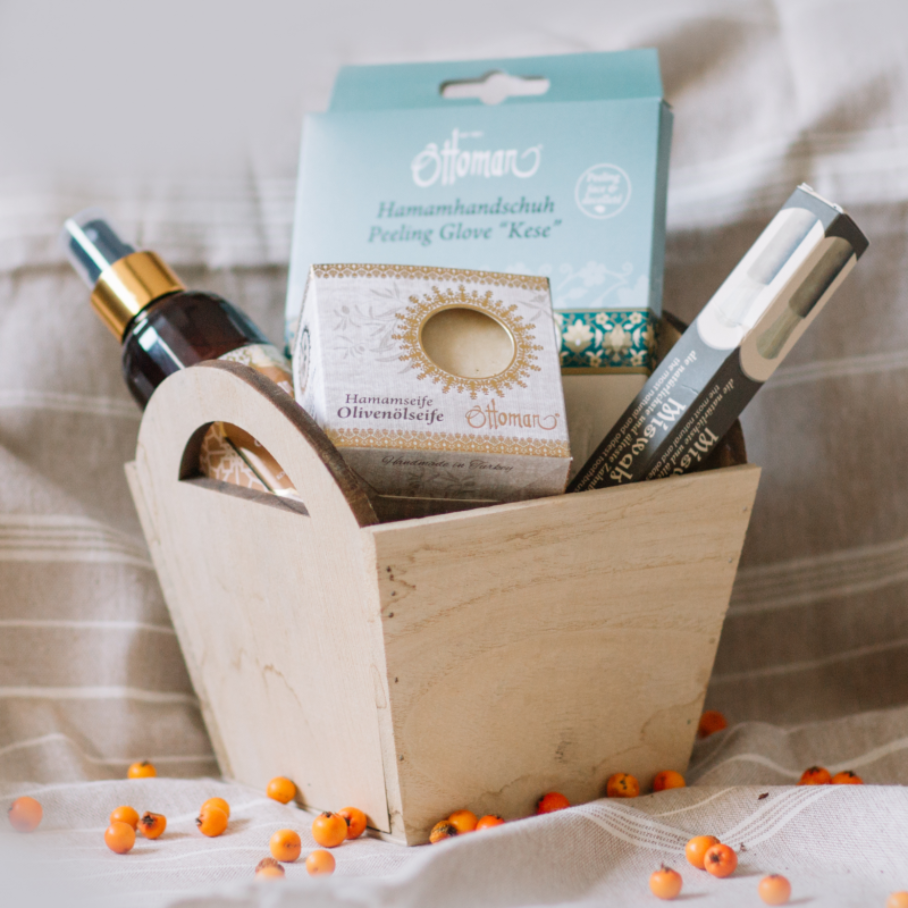 Four products, including a soap and an exfoliating glove, in a wooden box, with a striped cloth underneath.