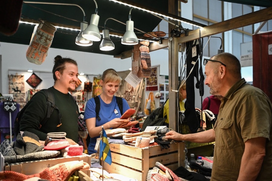 Drei lächelnde Personen in einer Kaufsituation, eine der Personen ist eine Frau, die Socken in den Händen hält. 